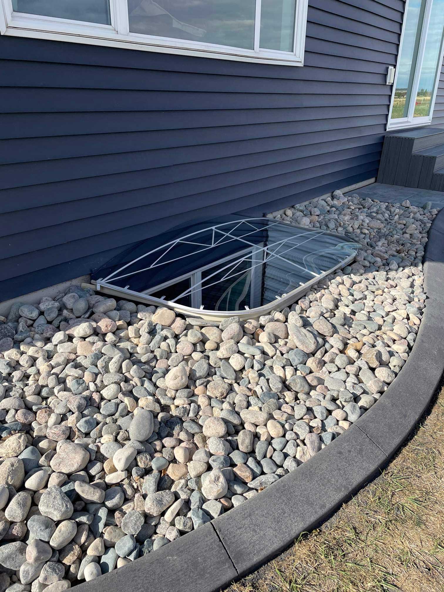 Glass basement window well with river rocks