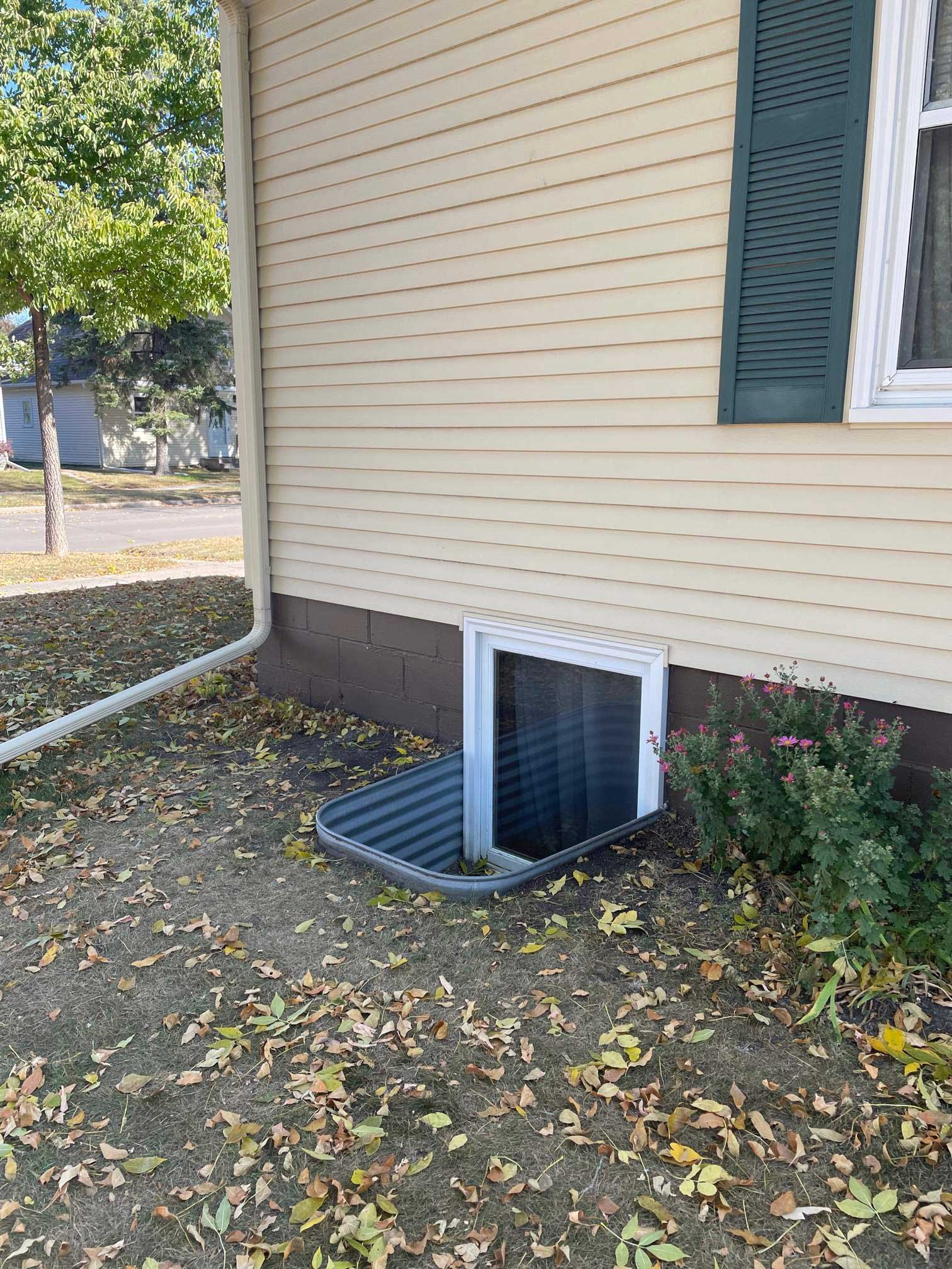 Basement window well beside beige house
