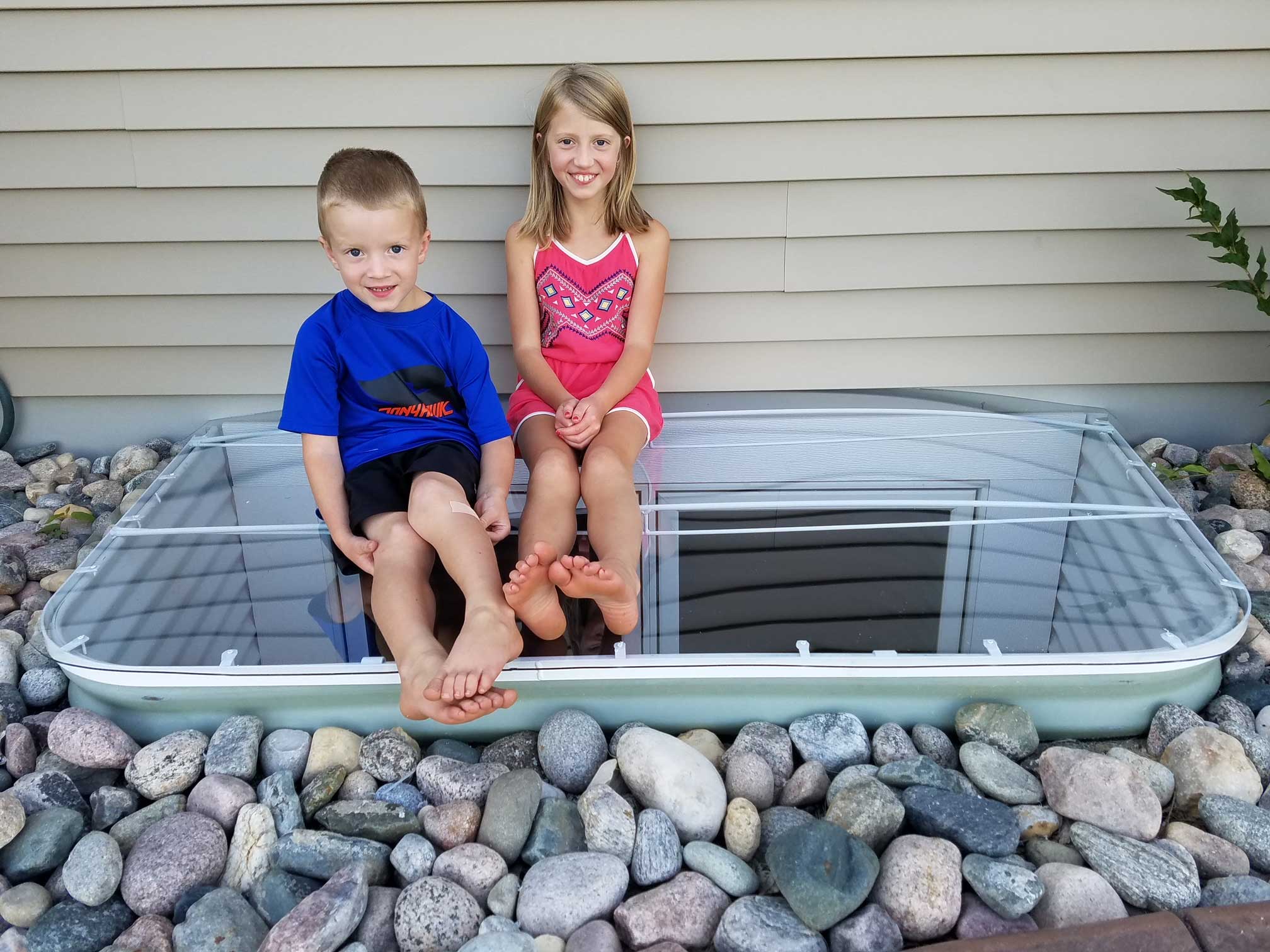 Two children sitting on basement window well cover