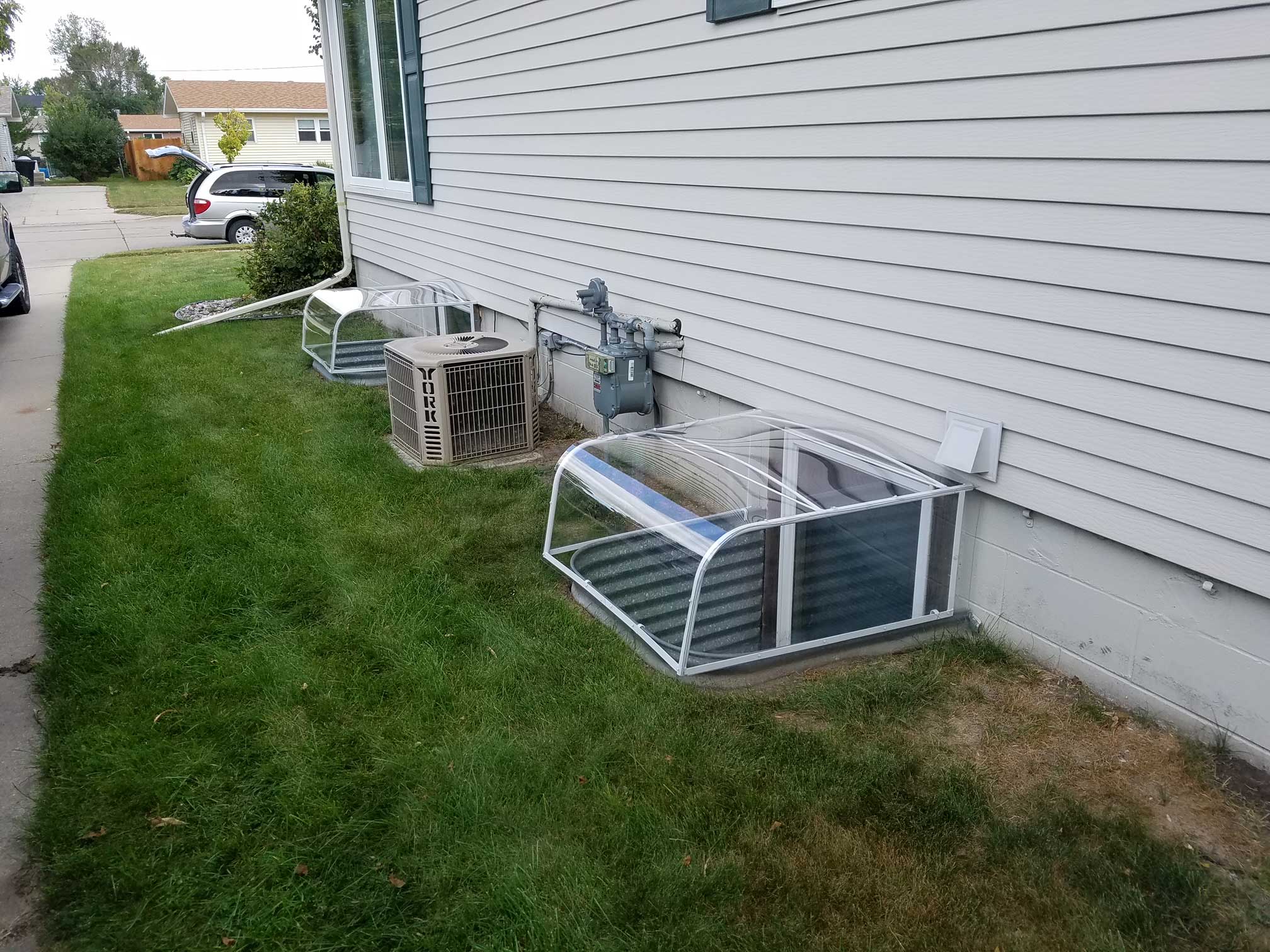 Two basement window well covers beside house