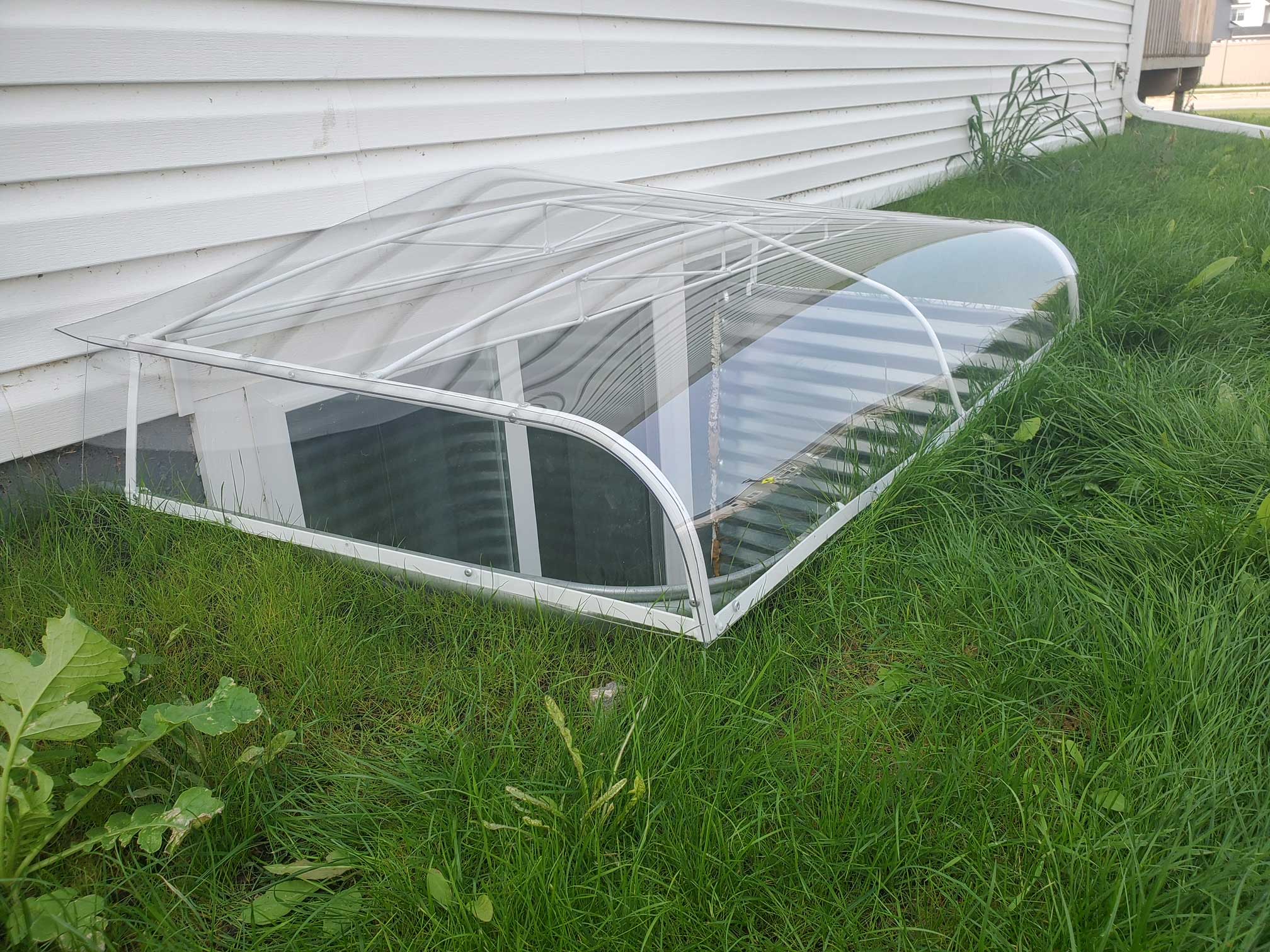 Clear acrylic basement window well cover on grass
