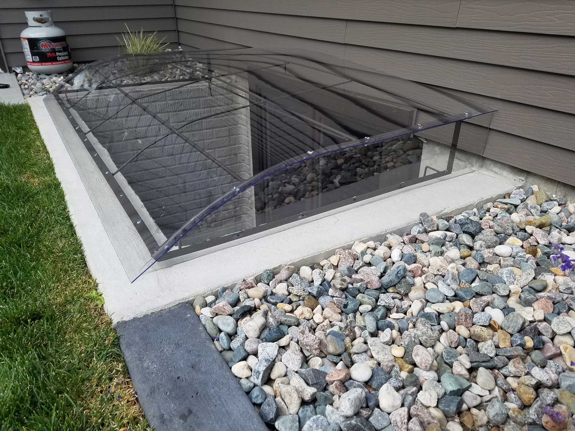 Clear arched window well cover beside house
