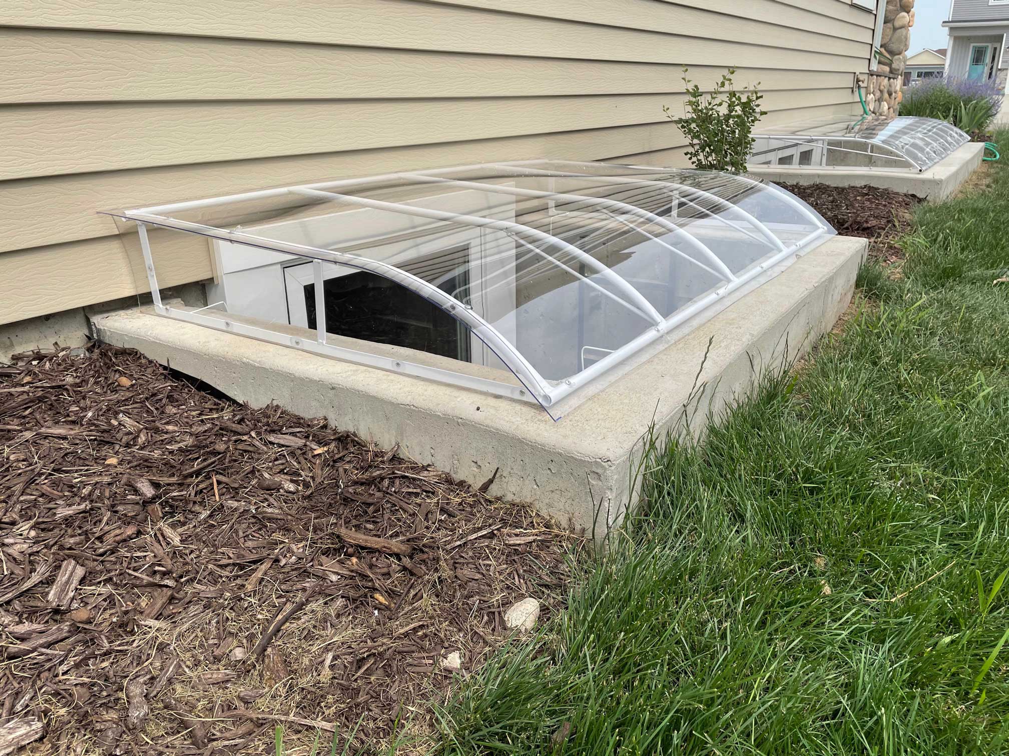 Curved plastic basement window well cover beside house