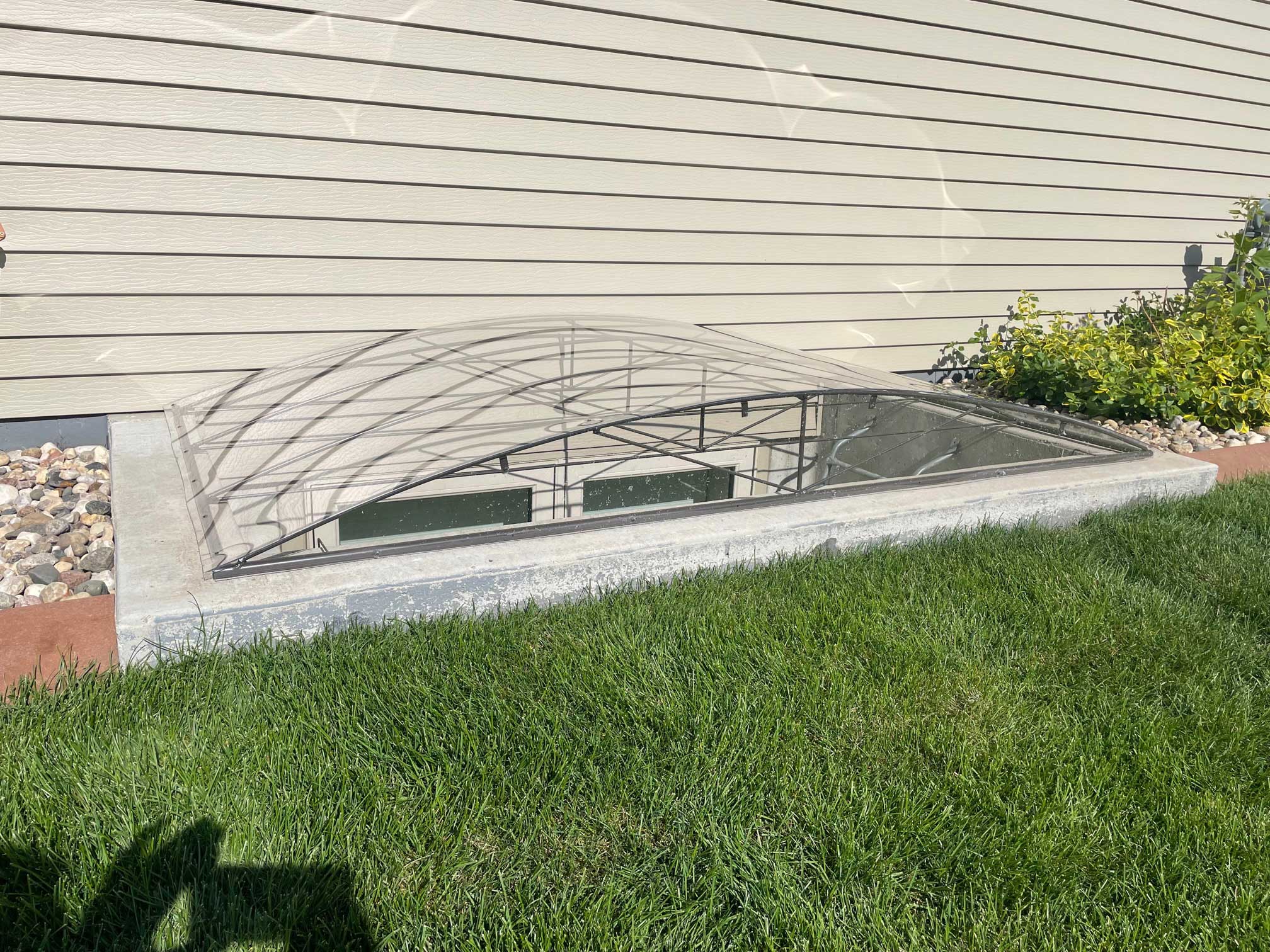 Clear arched window well cover beside house