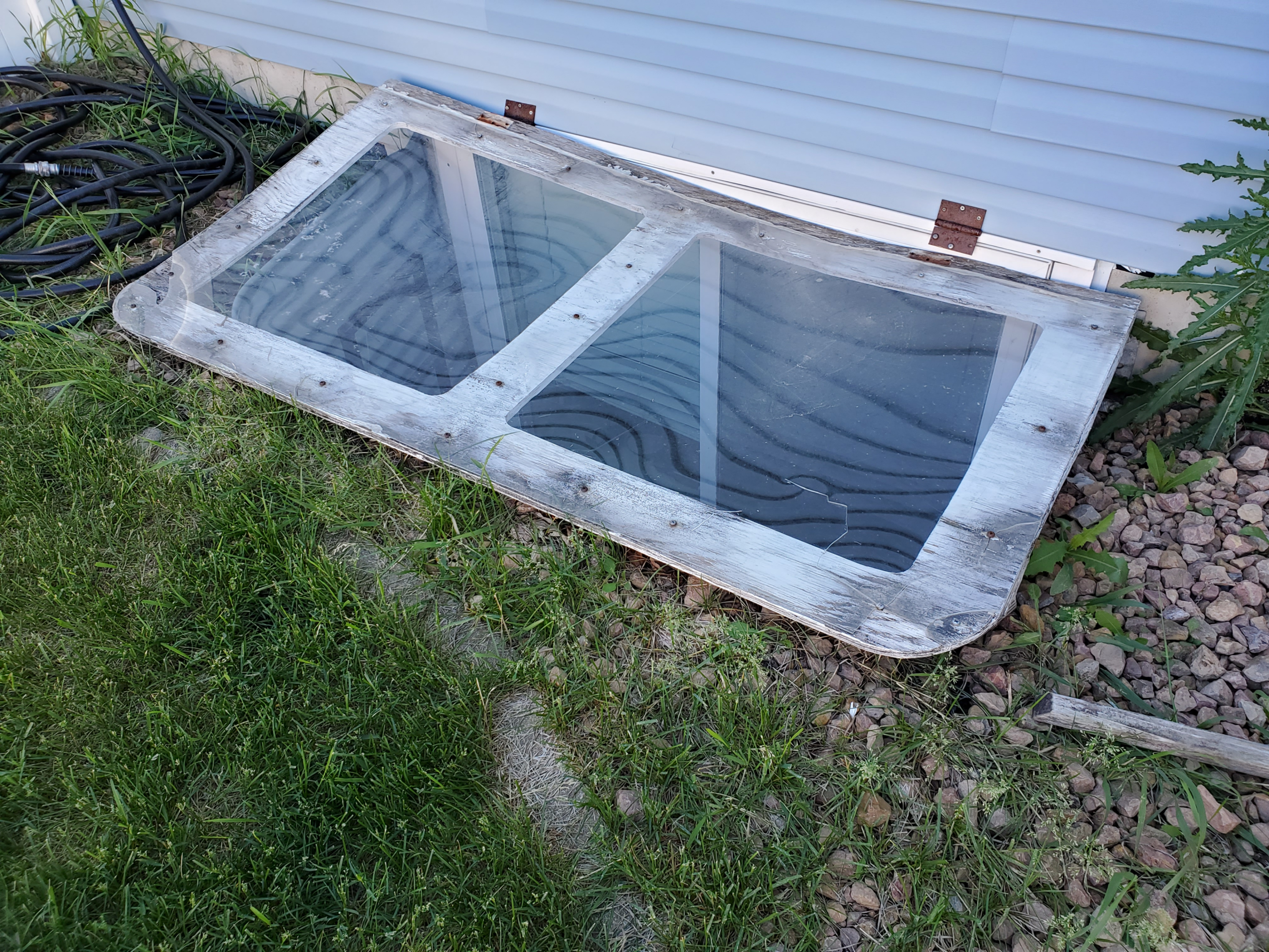 Basement window well cover leaning against house