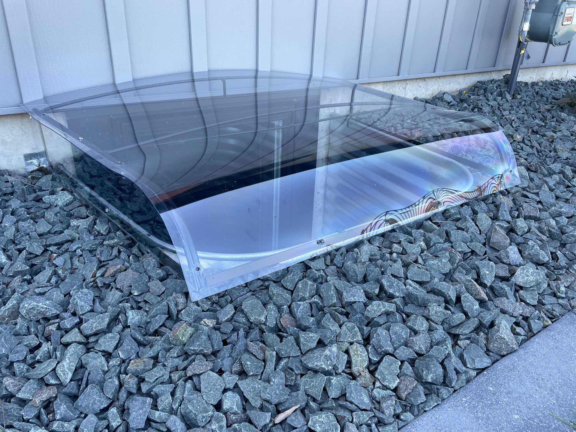 Curved clear window well cover over rocks