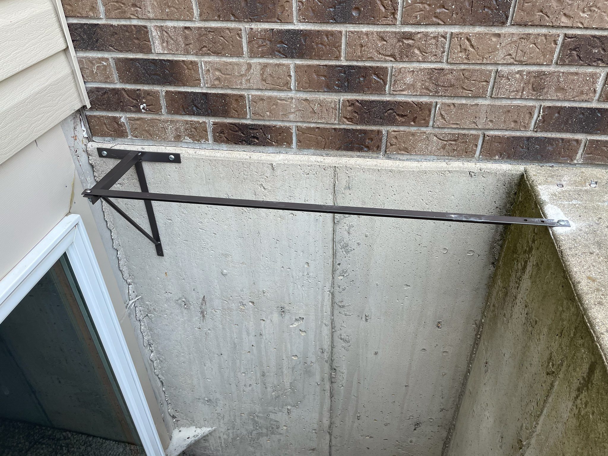 Metal support arm over basement window well